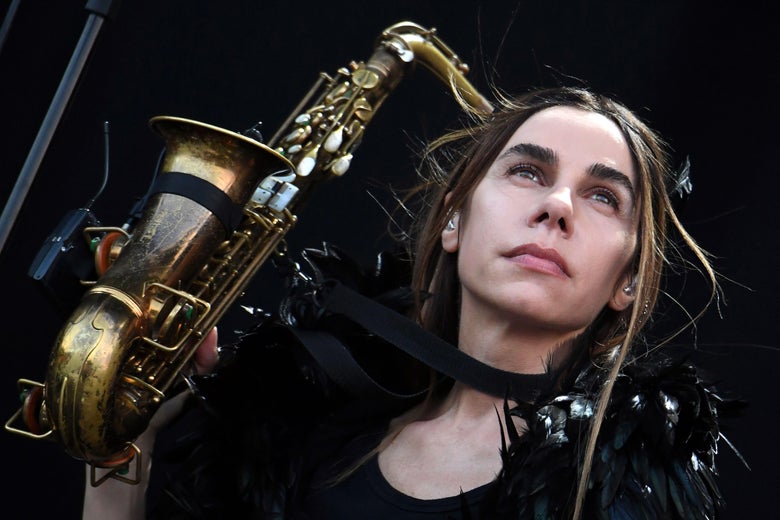 PJ Harvey, with an aloof stare and black-feathered get-up, holds a saxophone in front of a black background